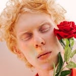 Close-up of a young albino man holding a red rose, showcasing vibrant colors.