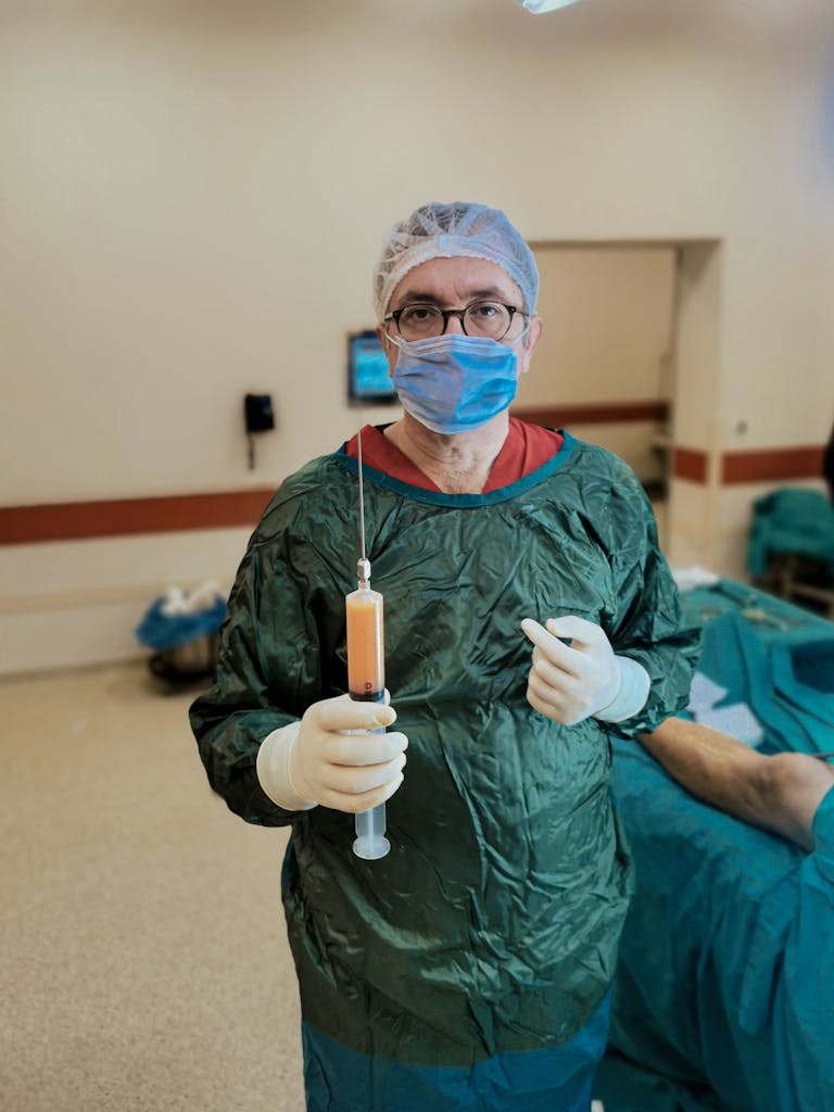 Plastic surgeon in scrubs holding a syringe during surgery in a hospital operating room.