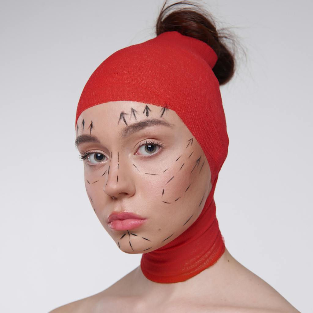 Portrait of a woman with surgery marks wearing a red head cover, symbolizing cosmetic surgery plans.
